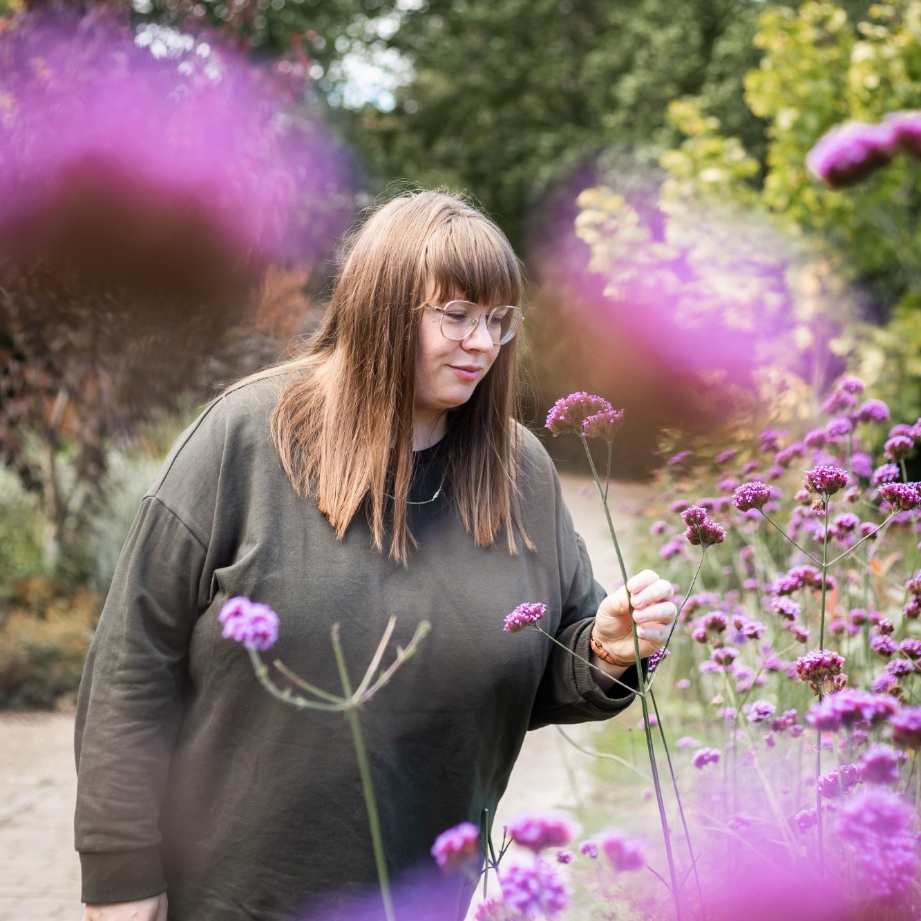 A woman gently touches purple flowers in a garden setting.