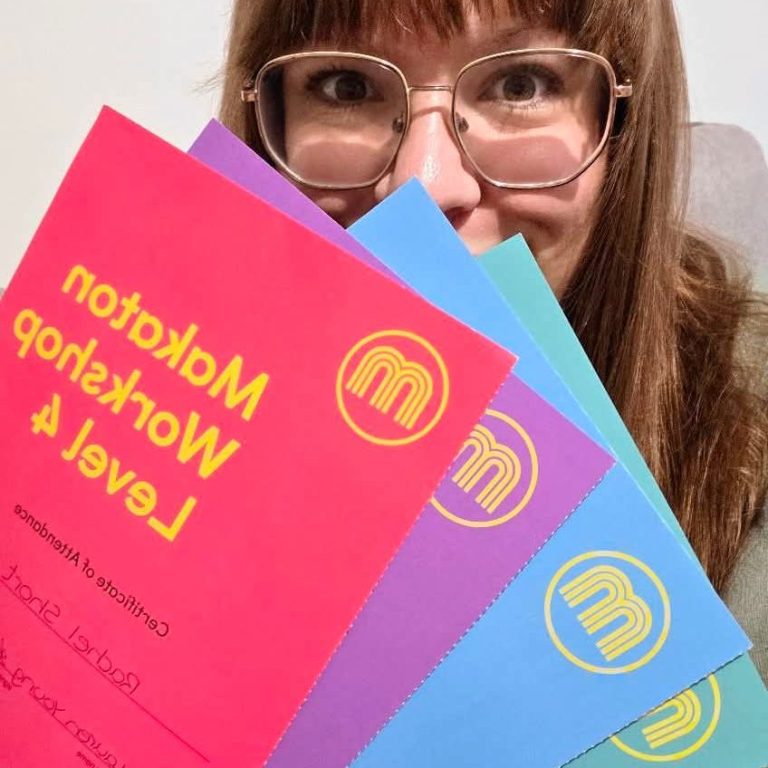Person with glasses holding colourful flyers for a workshop titled "Makaton Workshop".