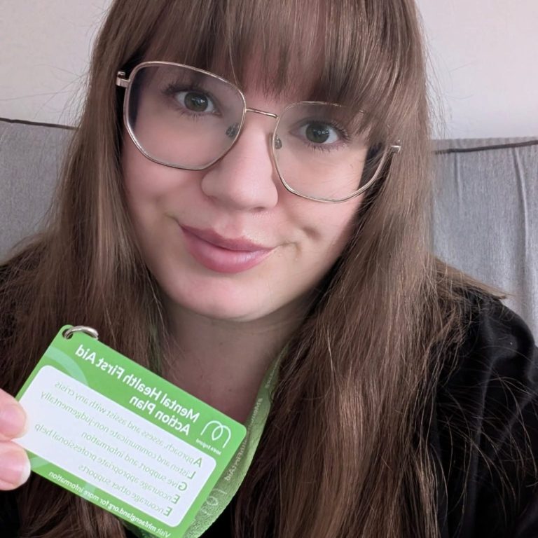 Young woman with glasses holding a green identification card, smiling at the camera.